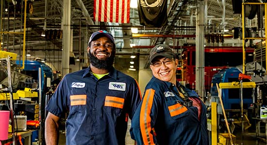 Two CapMetro mechanic with big smiles standing on the shop floor