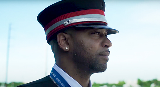 CapMetro rail conductor looking off into the distance as a MetroRail vehicle goes by behind him