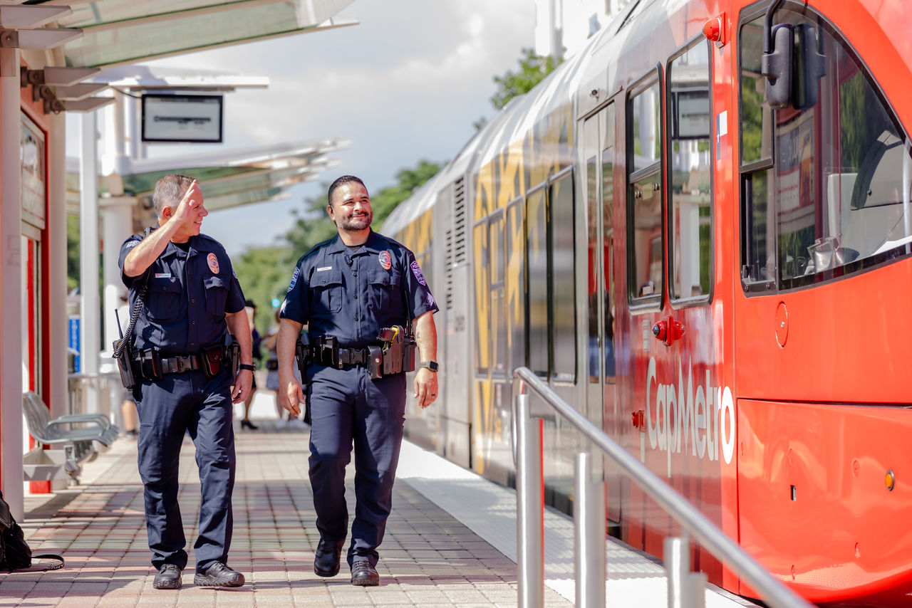 250712CapMetroPublicSafety_0089_web CapMetro Transit Police officers walking and waving to train operator.
